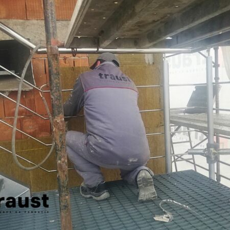 imagine cu muncitor din echipa Traust care monteaza vata bazaltica pe fatada unei cladiri